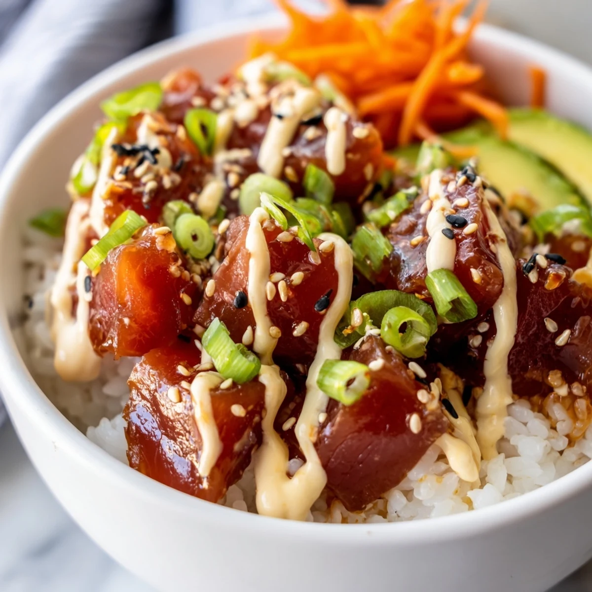 Fresh diced tuna marinated in spicy sriracha and sesame oil rests on fluffy sushi rice, topped with creamy avocado slices and a drizzle of spicy mayo. Spicy Tuna Poke Bowl