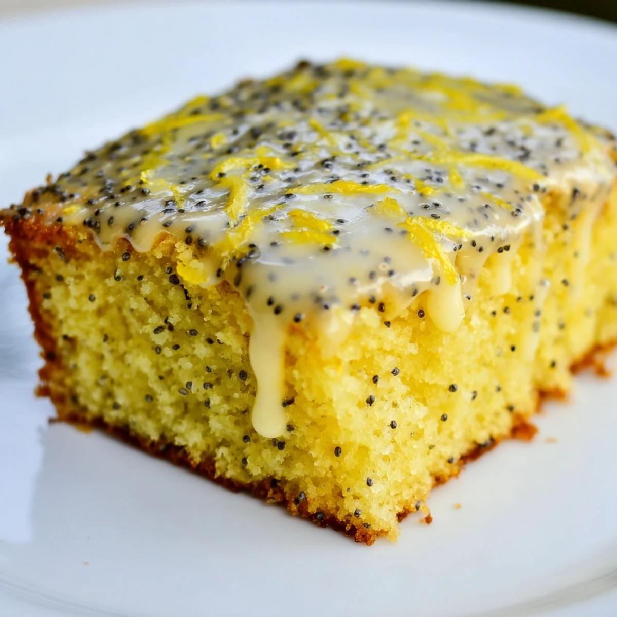 Freshly baked Lemon Drizzle Traybake with Poppy Seeds squares on a wooden board, glistening with tangy glaze.