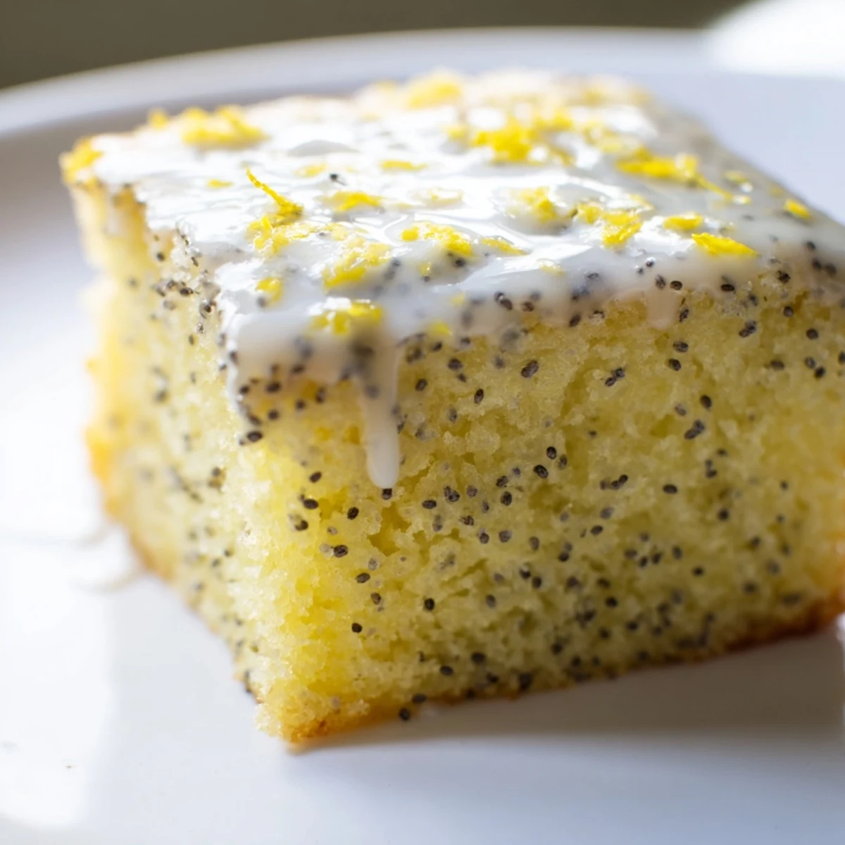 A slice of Lemon Drizzle Traybake with Poppy Seeds on a plate, served with a dollop of creamy Greek yogurt.