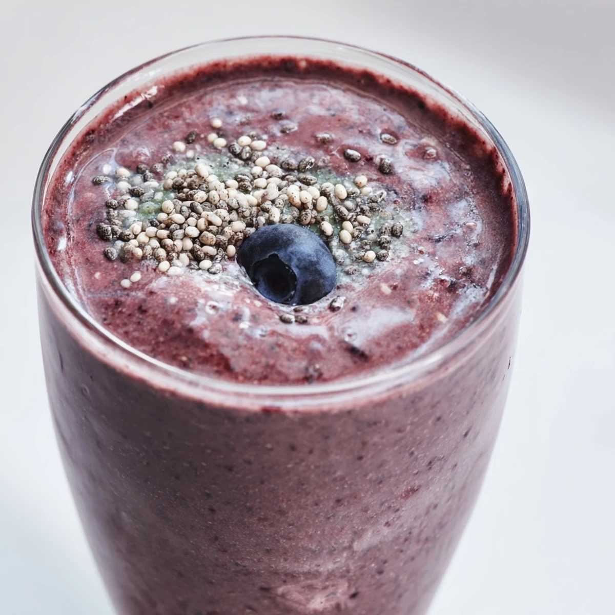 Two tall glasses of Winter Berry Smoothie with Spinach and Banana, topped with a few whole berries and chia seeds, served with a striped straw.
