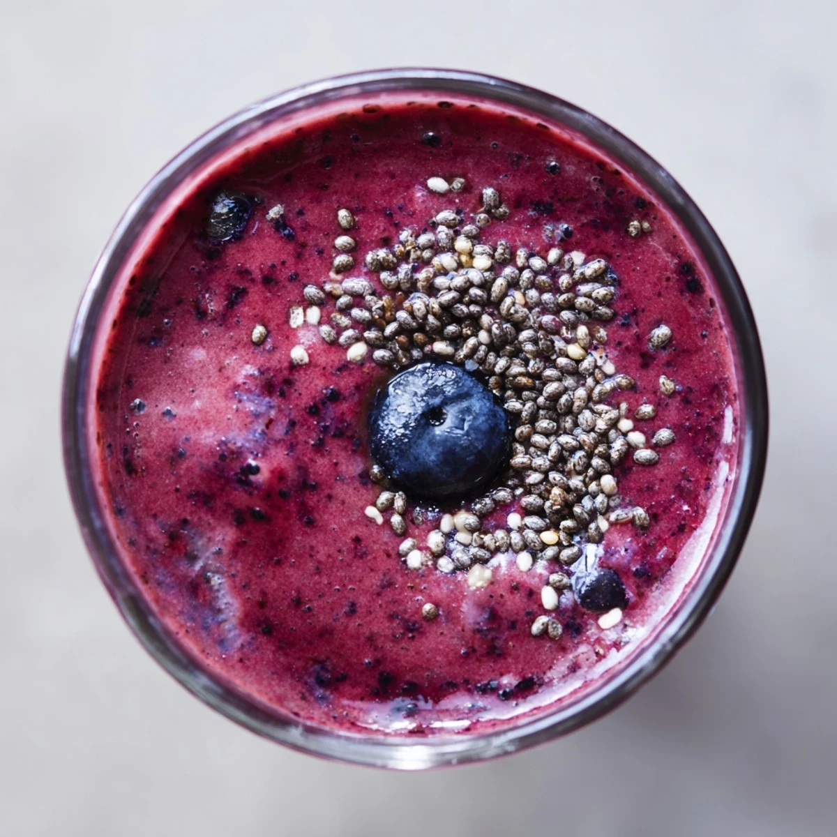 Close-up of a vibrant Winter Berry Smoothie with Spinach and Banana, showcasing a thick, creamy purple blend flecked with fresh green spinach.