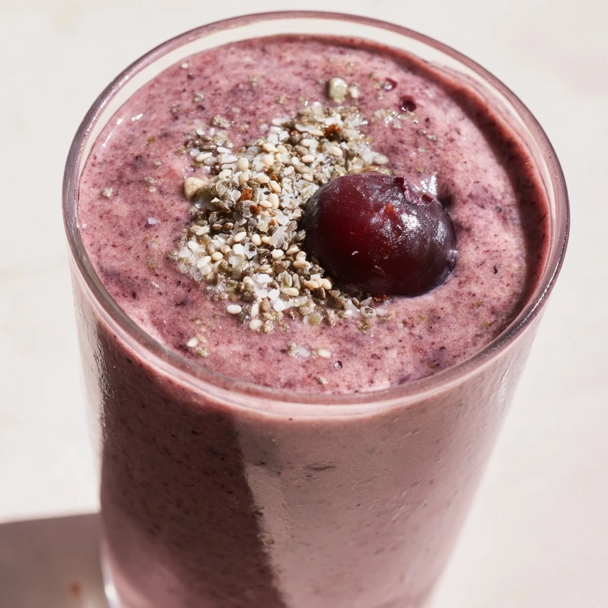 A freshly blended Winter Berry Smoothie with Spinach and Banana, poured into a clear glass beside frozen berries and a sliced banana.