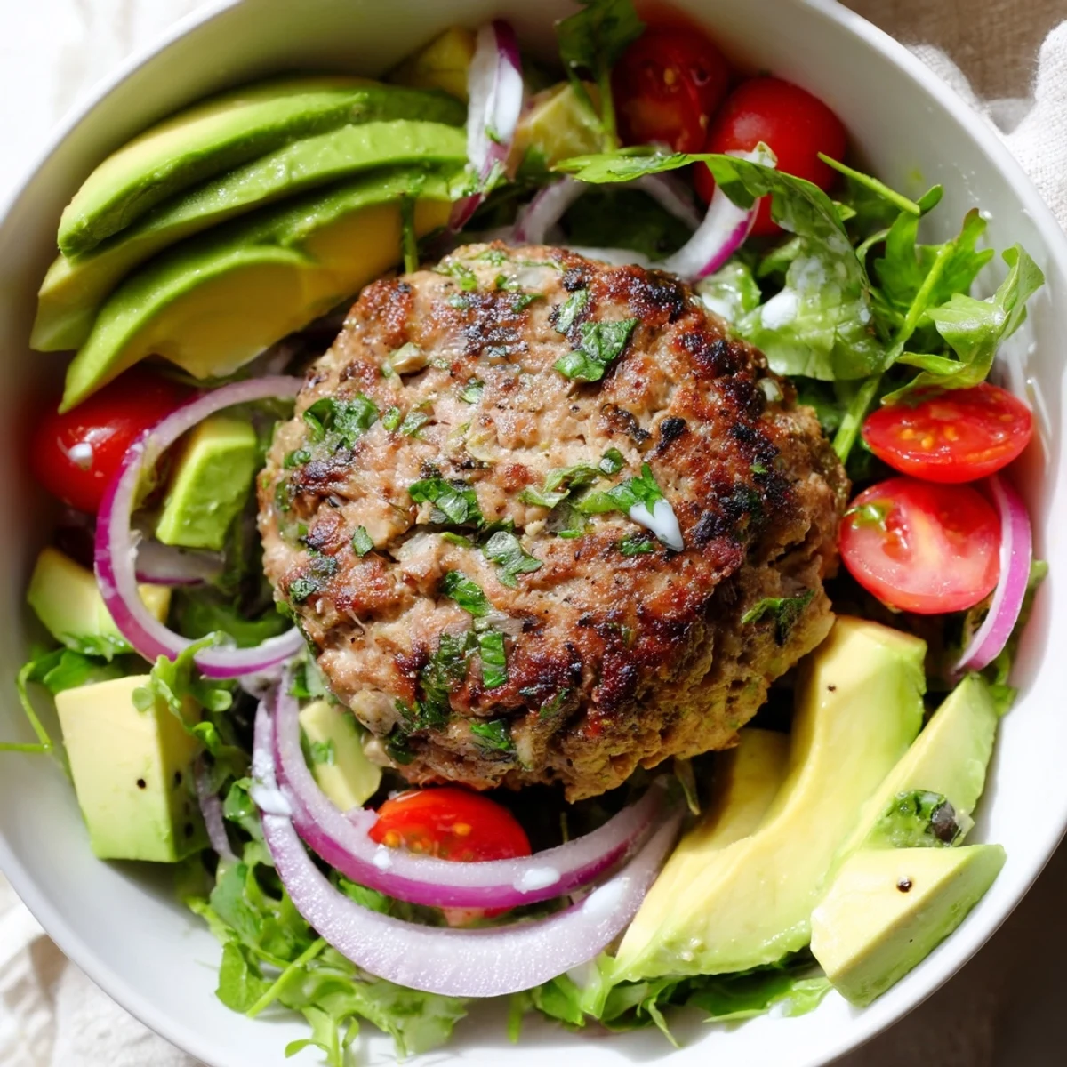 Juicy turkey burger patties rest on a vibrant salad base with cherry tomatoes, cucumber, and creamy avocado, drizzled with a tangy Greek yogurt dressing.