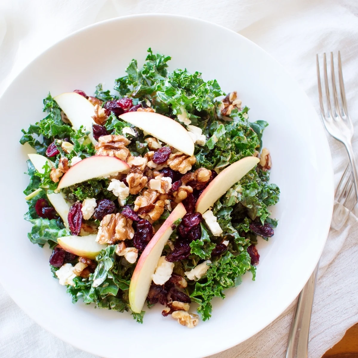 A close-up of the Winter Kale Salad with Cranberries, highlighting glossy dressing-coated leaves, bright apple slices, and golden toasted nuts.