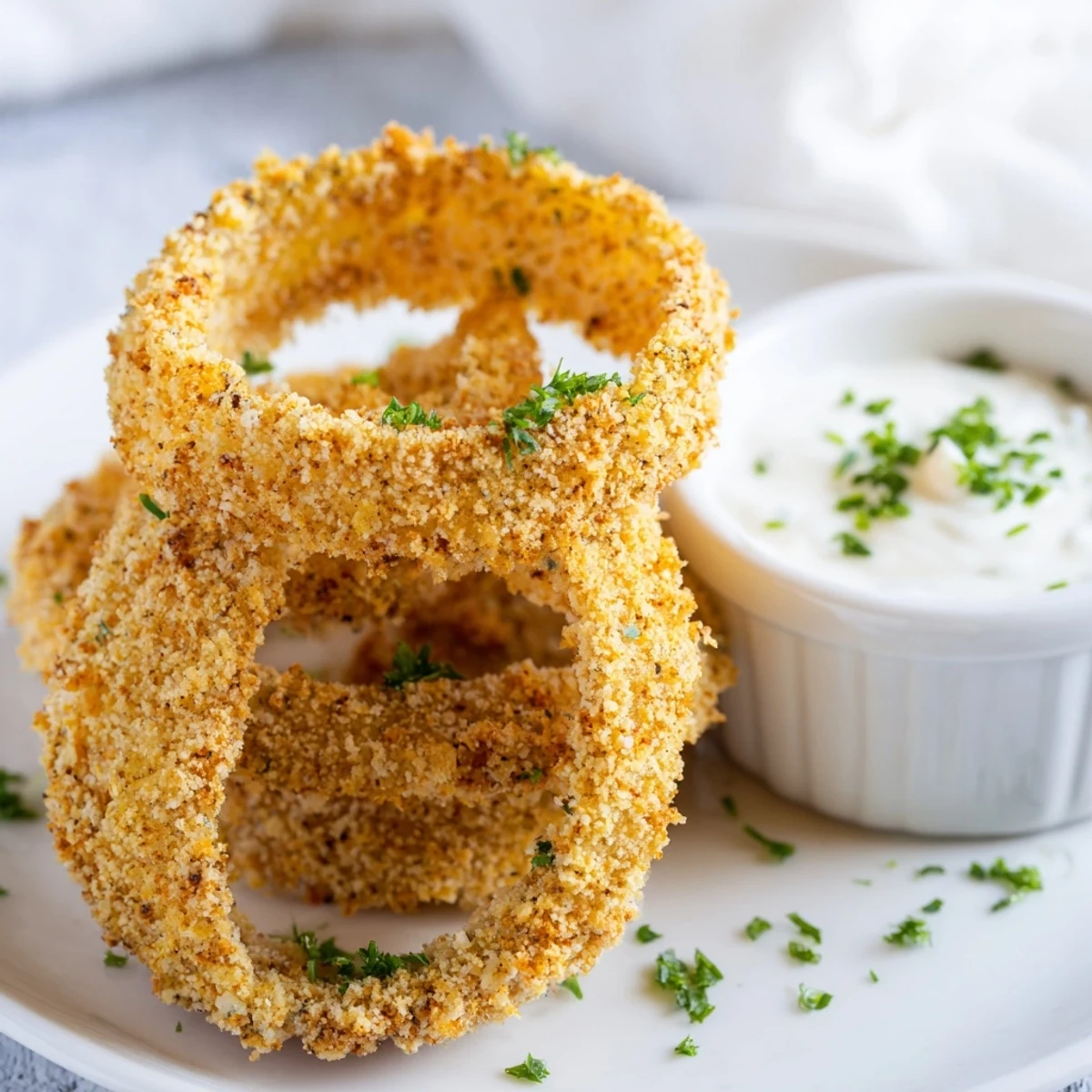 Crispy Baked Onion Rings with Ranch piled high on a platter, golden brown and sprinkled with fresh parsley.
