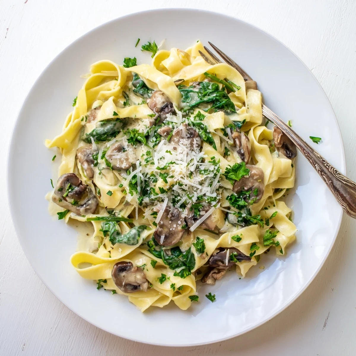 Creamy Mushroom and Spinach Pasta is served steaming in a shallow white bowl, topped with fresh parsley and grated Parmesan cheese.