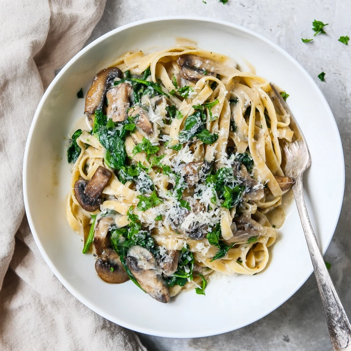 A skillet of Creamy Mushroom and Spinach Pasta is ready to serve, garnished with parsley and a glass of white wine.