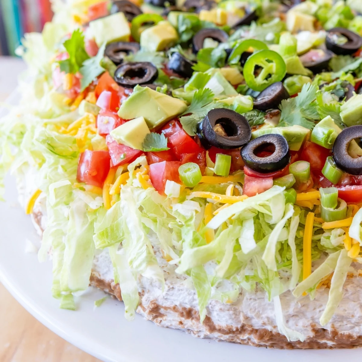 Colorful layers of refried beans, seasoned cream cheese, salsa, and shredded lettuce in Ultimate Layered Taco Dip, served with crispy tortilla chips.