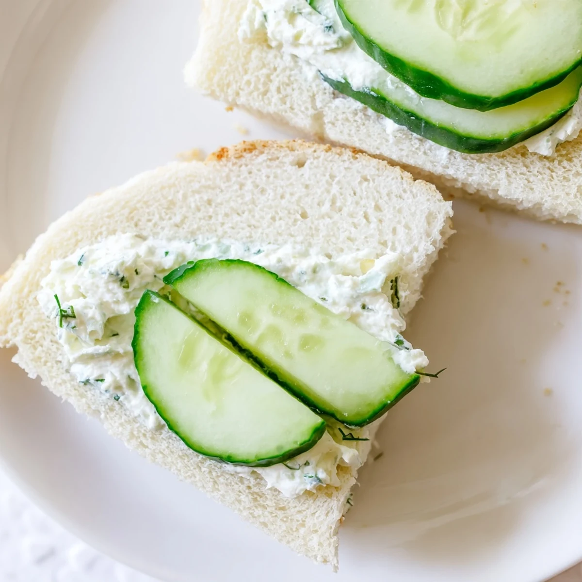 Cucumber sandwiches with herb cream cheese displayed on a white plate, featuring thin cucumber slices and a herb spread.