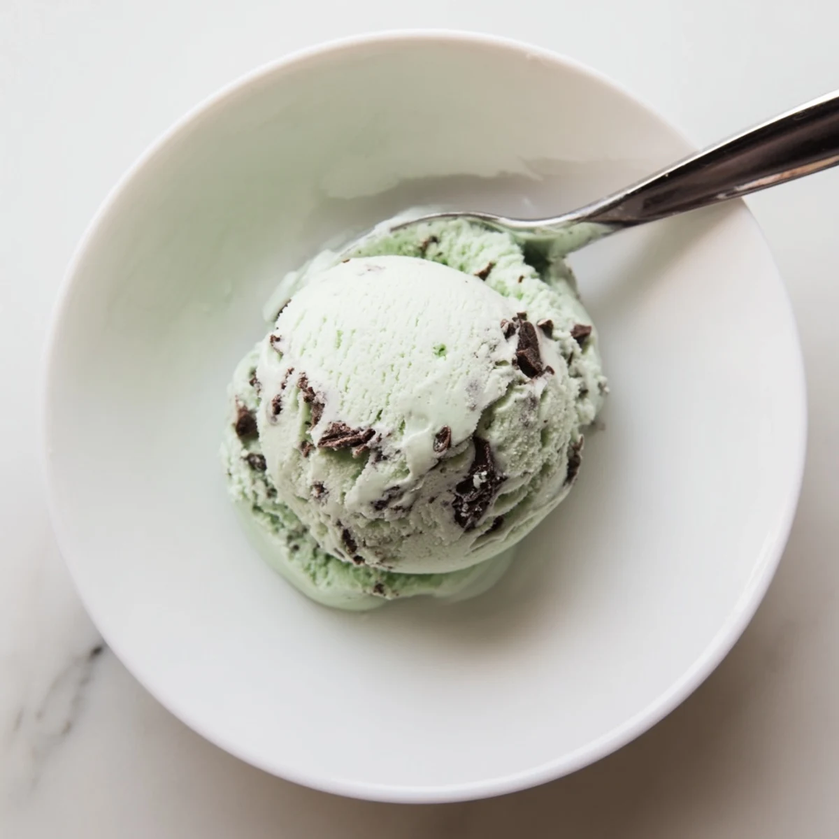 Homemade Mint Chocolate Chip Ice Cream overflowing a waffle cone, garnished with fresh mint leaves.  