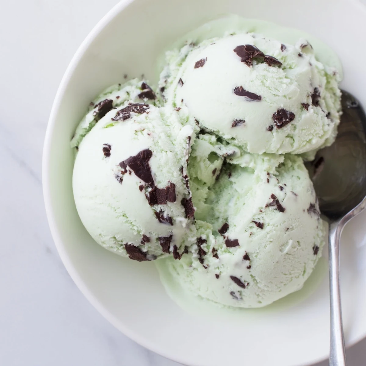 Indulgent Mint Chocolate Chip Ice Cream scoop in a glass, showing smooth texture and dark chocolate pieces.
