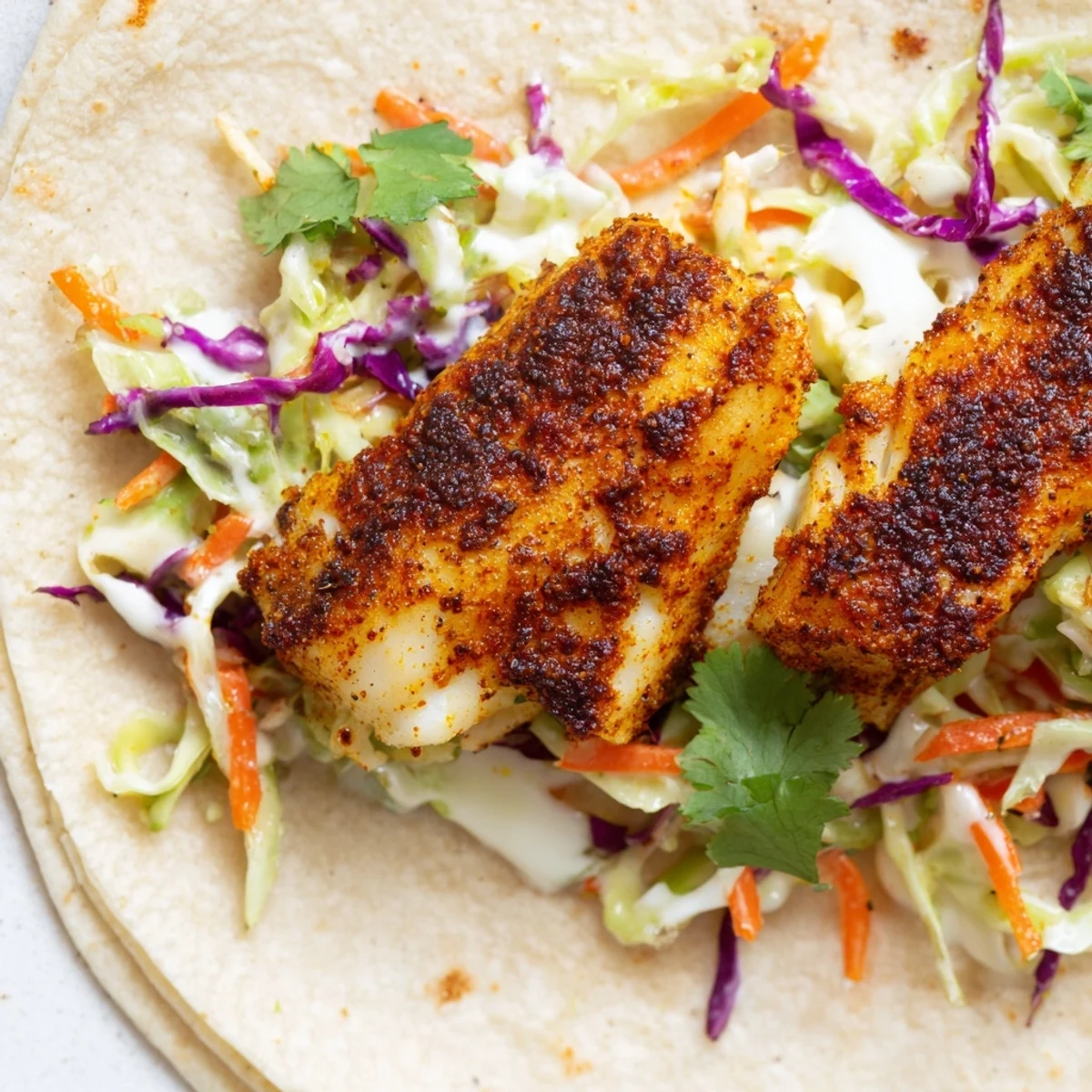Overhead view of Cajun Spiced Fish Tacos with Slaw, featuring generously filled tortillas topped with fresh cilantro and lime wedges on the side.