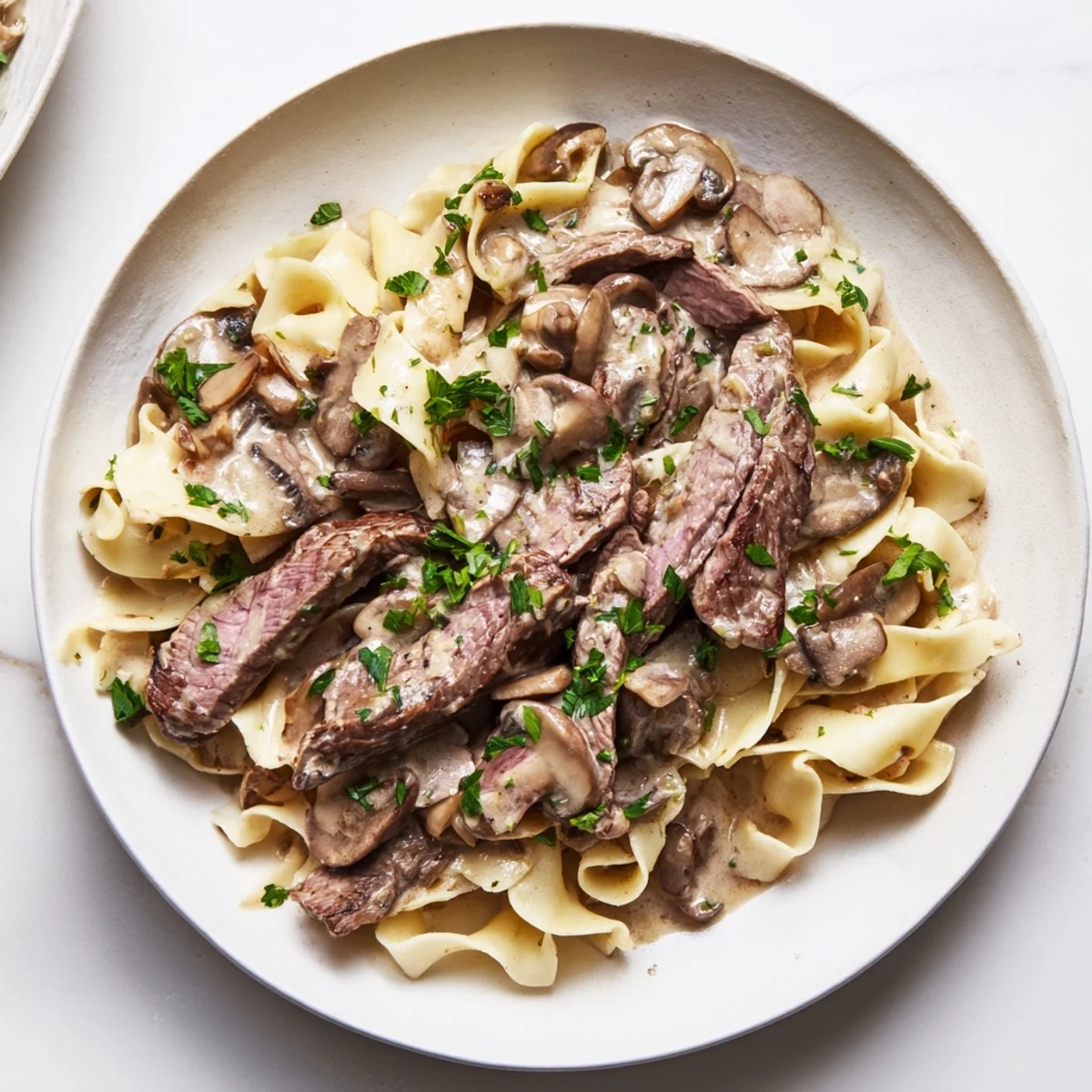 A close-up of Beef Stroganoff with egg noodles, garnished with fresh parsley, ready to serve.