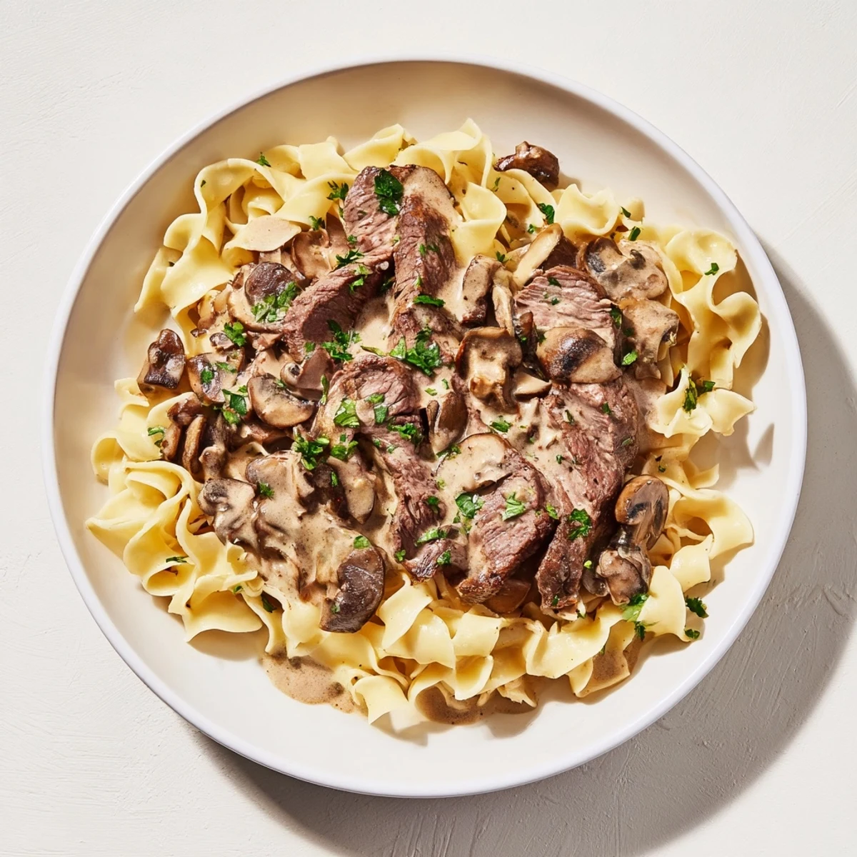 Tender beef and savory mushrooms in rich sauce piled high on fluffy egg noodles for Beef Stroganoff.