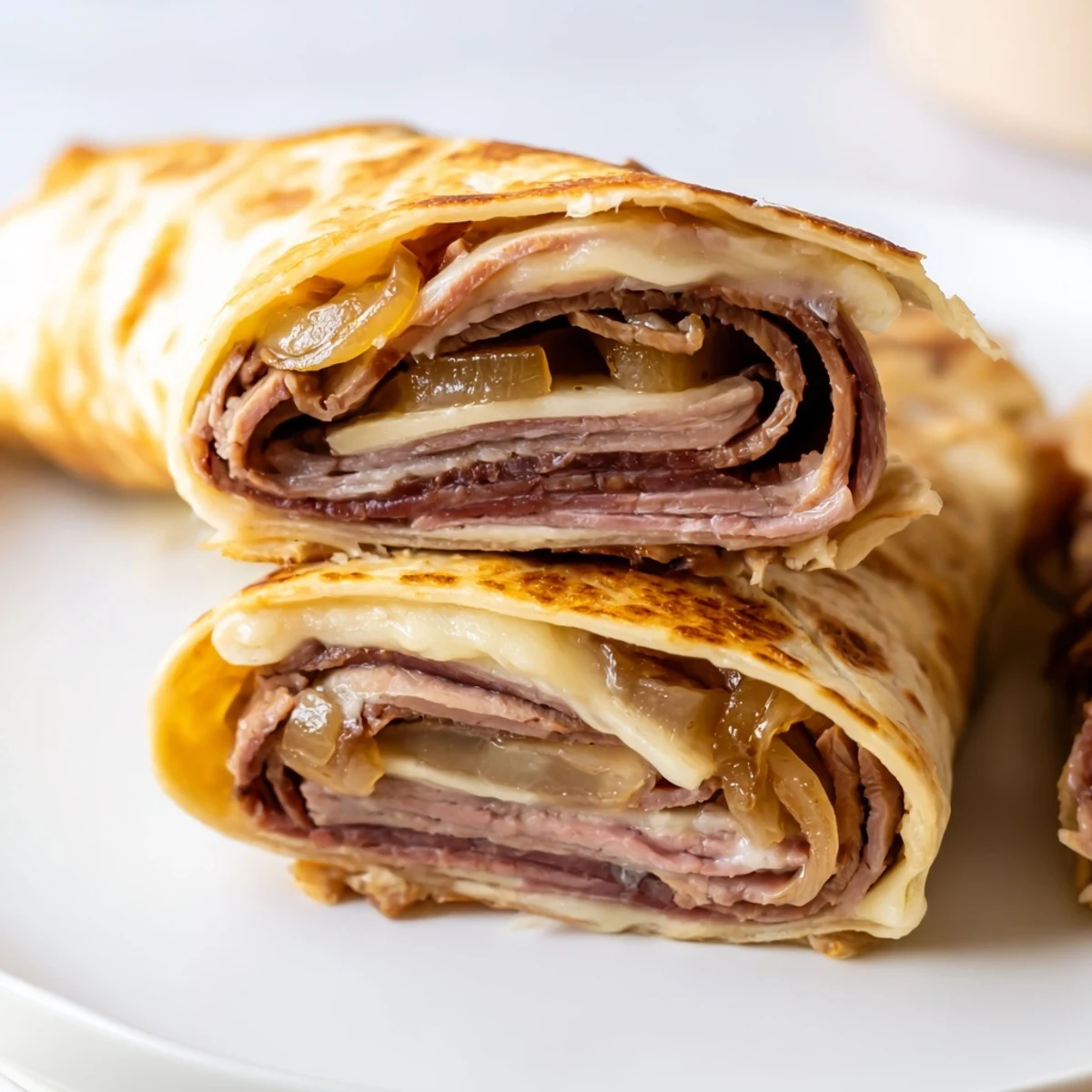 Golden-brown Easy French Dip Tortilla Roll Ups filled with roast beef, melty provolone, and caramelized onions, served with warm au jus on the side.