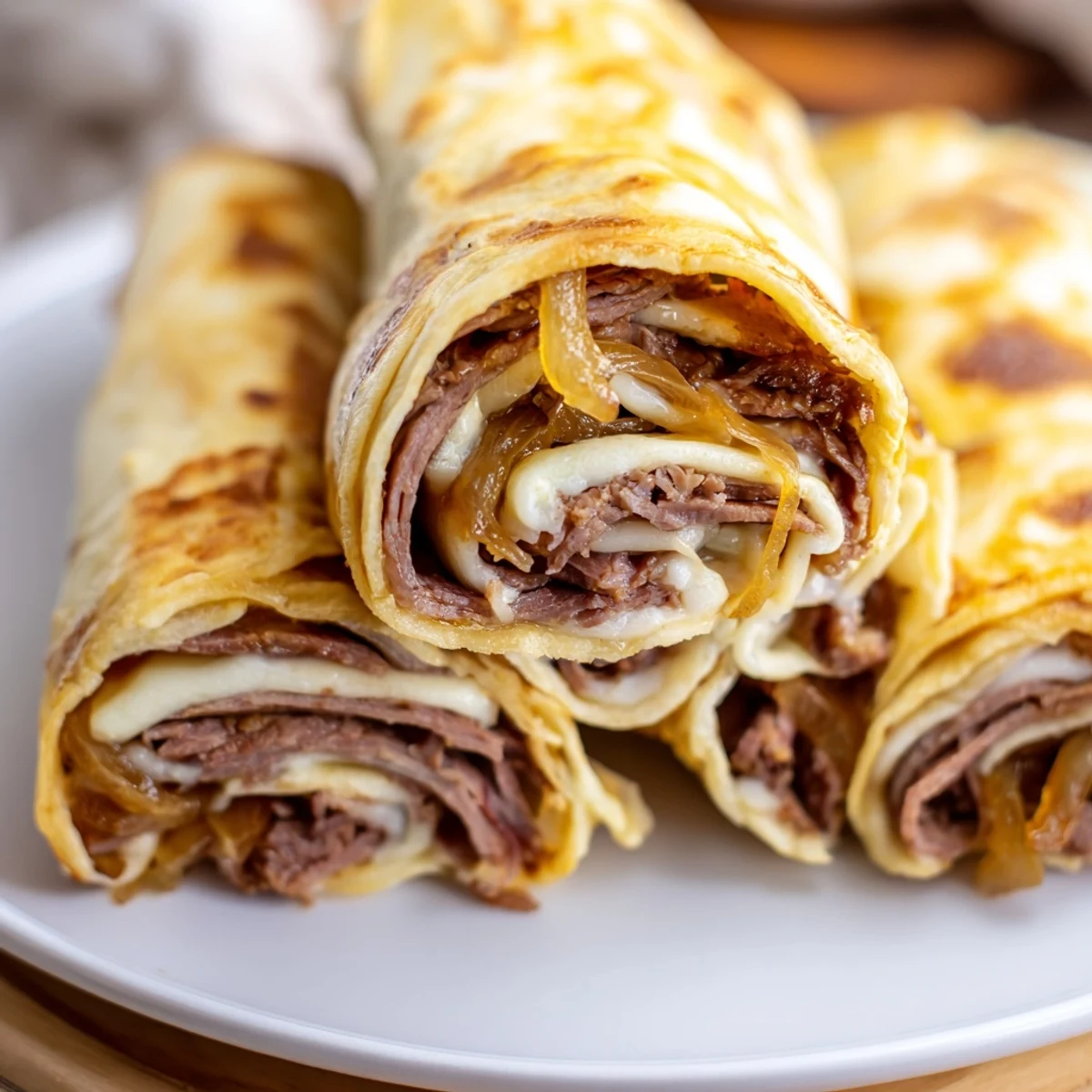 Crisp-baked Easy French Dip Tortilla Roll Ups on a white plate, featuring tender roast beef and melted cheese, ready for dipping in savory broth.