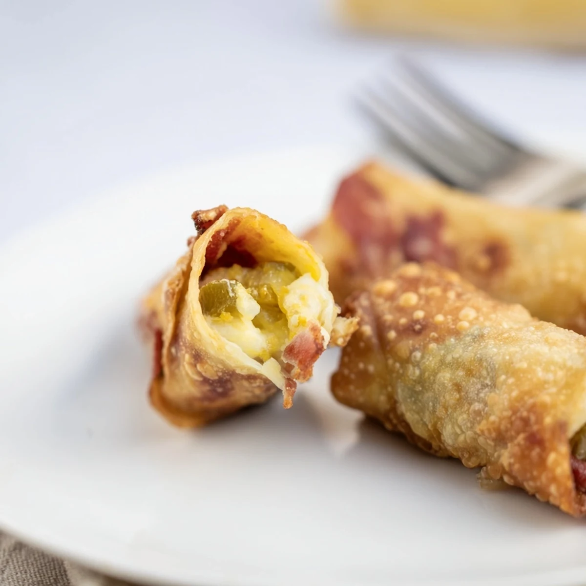 Golden brown Bacon Jalapeno Popper Eggrolls are displayed on a plate, showing crispy exterior and creamy filling.