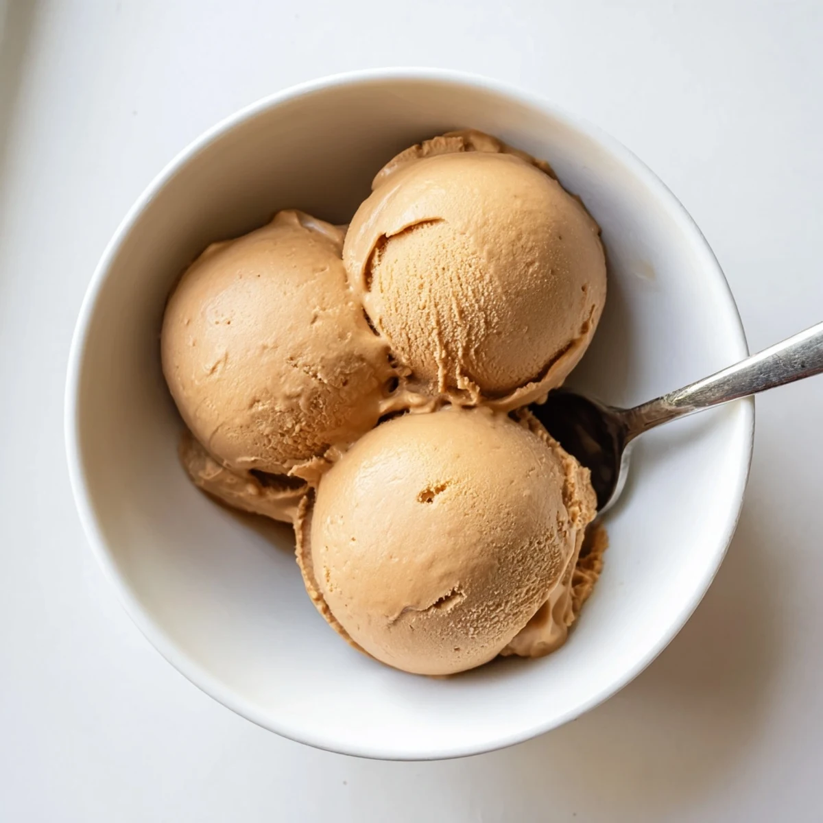 Creamy Hojicha Ice Cream scooped into a bowl with toasted sesame seeds and caramel drizzle.  