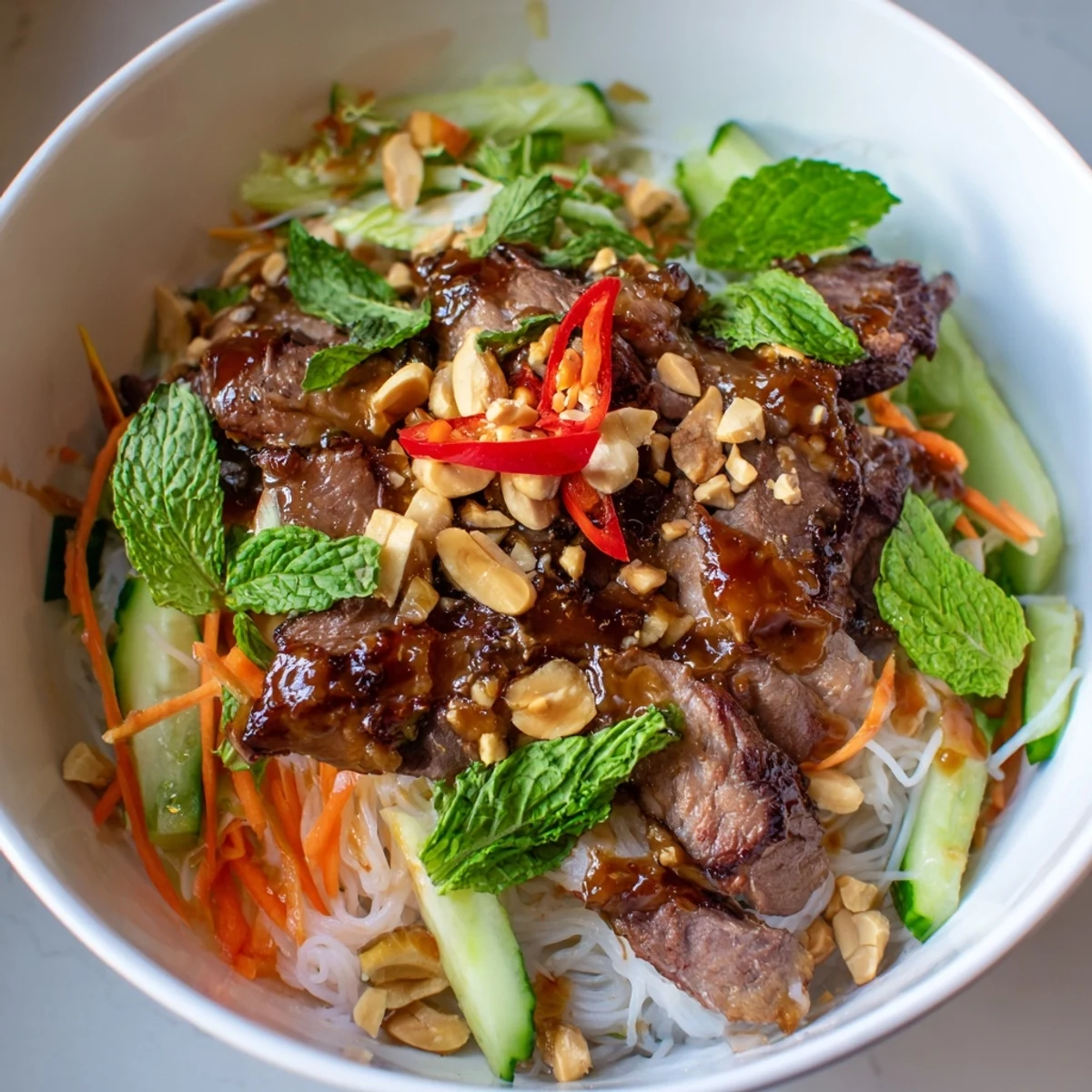 A close-up of Bun Bo Xao, sautéed beef glistening beside crisp veggies and rice noodles in a Vietnamese salad bowl.