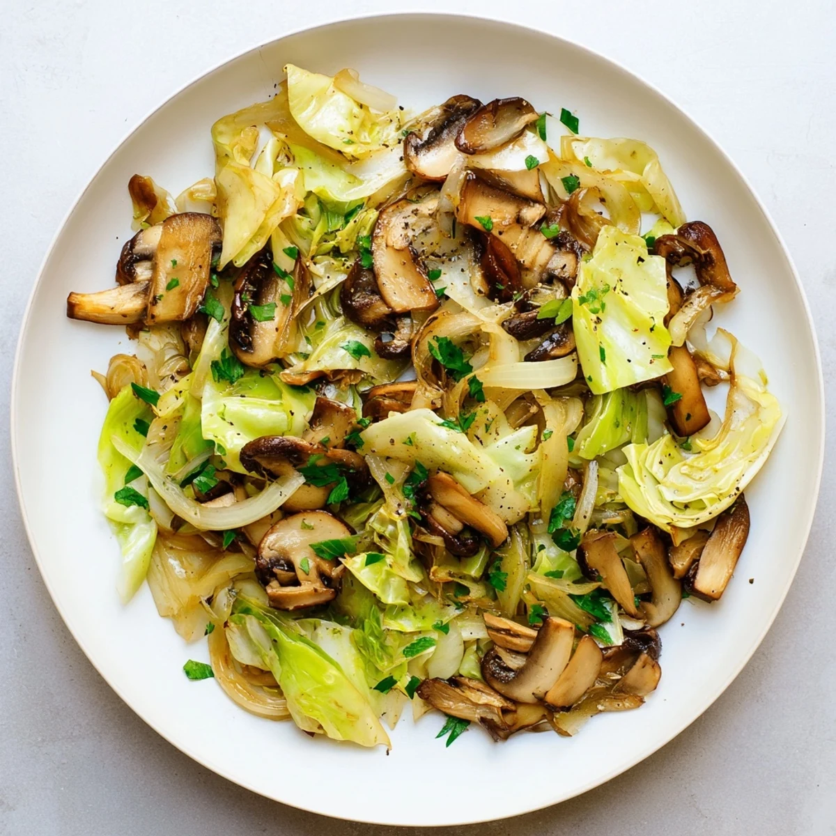 Tender cabbage and browned mushrooms tossed with olive oil and herbs in skillet.