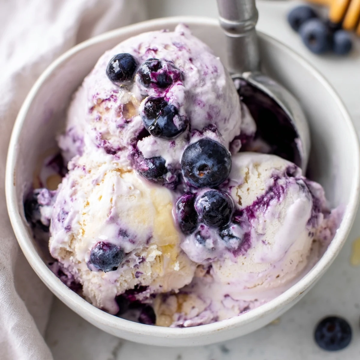 A scoop of creamy Blueberry Cottage Cheese Ice Cream in a white bowl, topped with fresh blueberries and a drizzle of honey.  