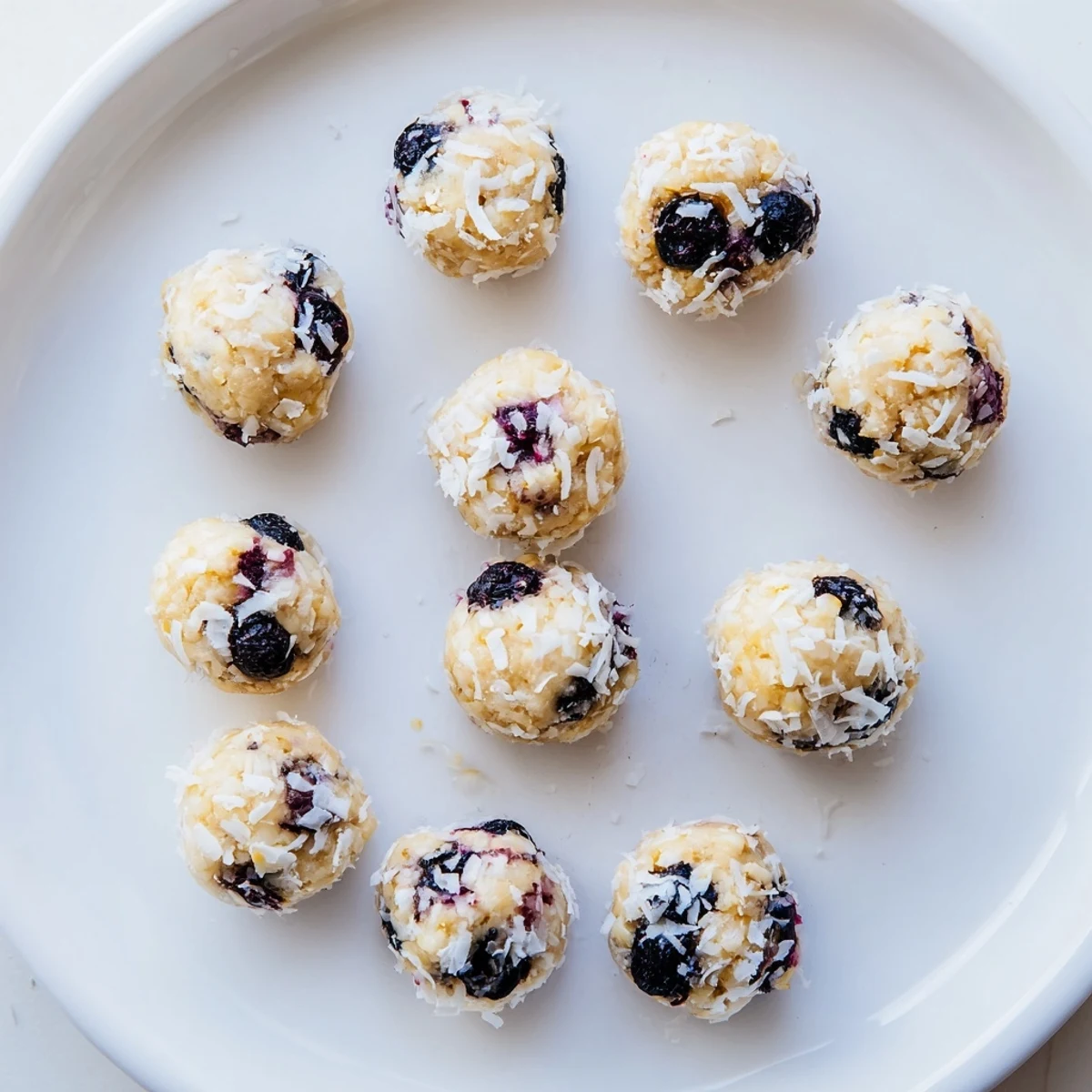 Fresh Lemon Blueberry Cottage Cheese Protein Bites rolled in coconut on a white plate.