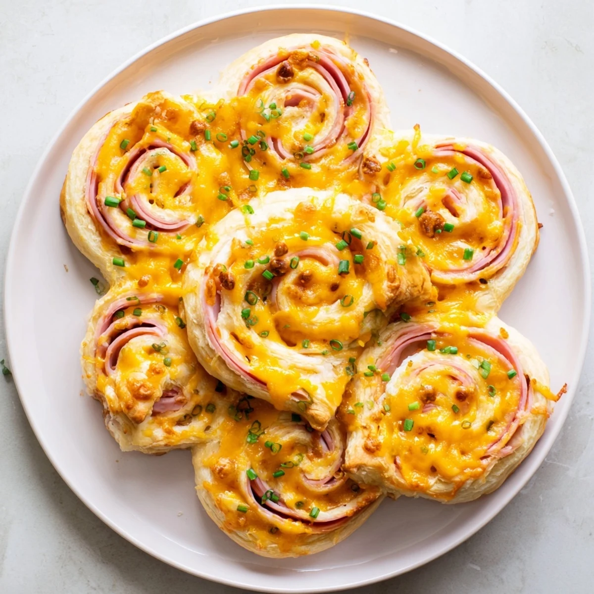 Golden Easter Ham Cheddar Pinwheels arranged on a white platter with fresh chives and a small bowl of Dijon mustard.