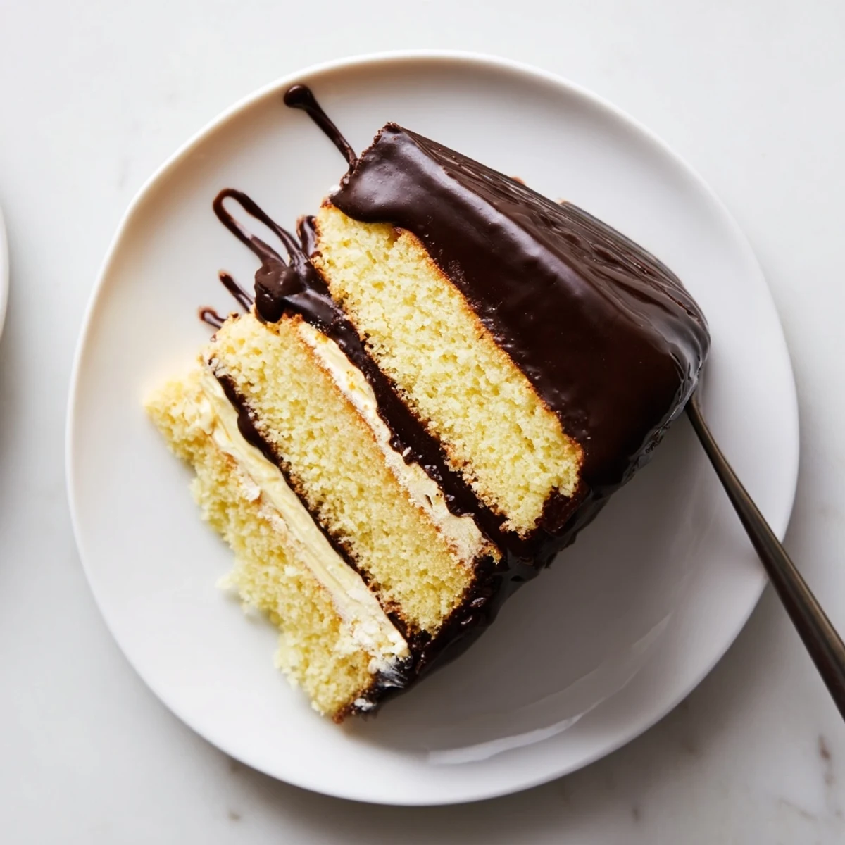 Homemade classic Boston cream pie slice revealing fluffy vanilla cake layers with rich custard filling and chocolate ganache topping