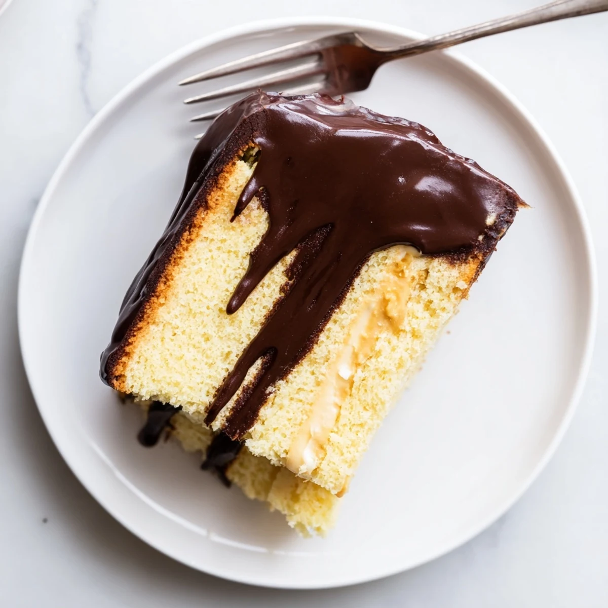 Decadent classic Boston cream pie plated on white dessert dish showing cross section of yellow cake smooth custard and dark chocolate frosting