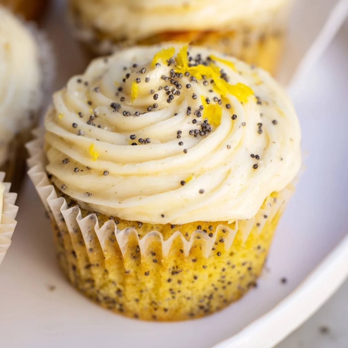 Golden lemon poppy seed cupcakes topped with fluffy cream cheese frosting and fresh zest