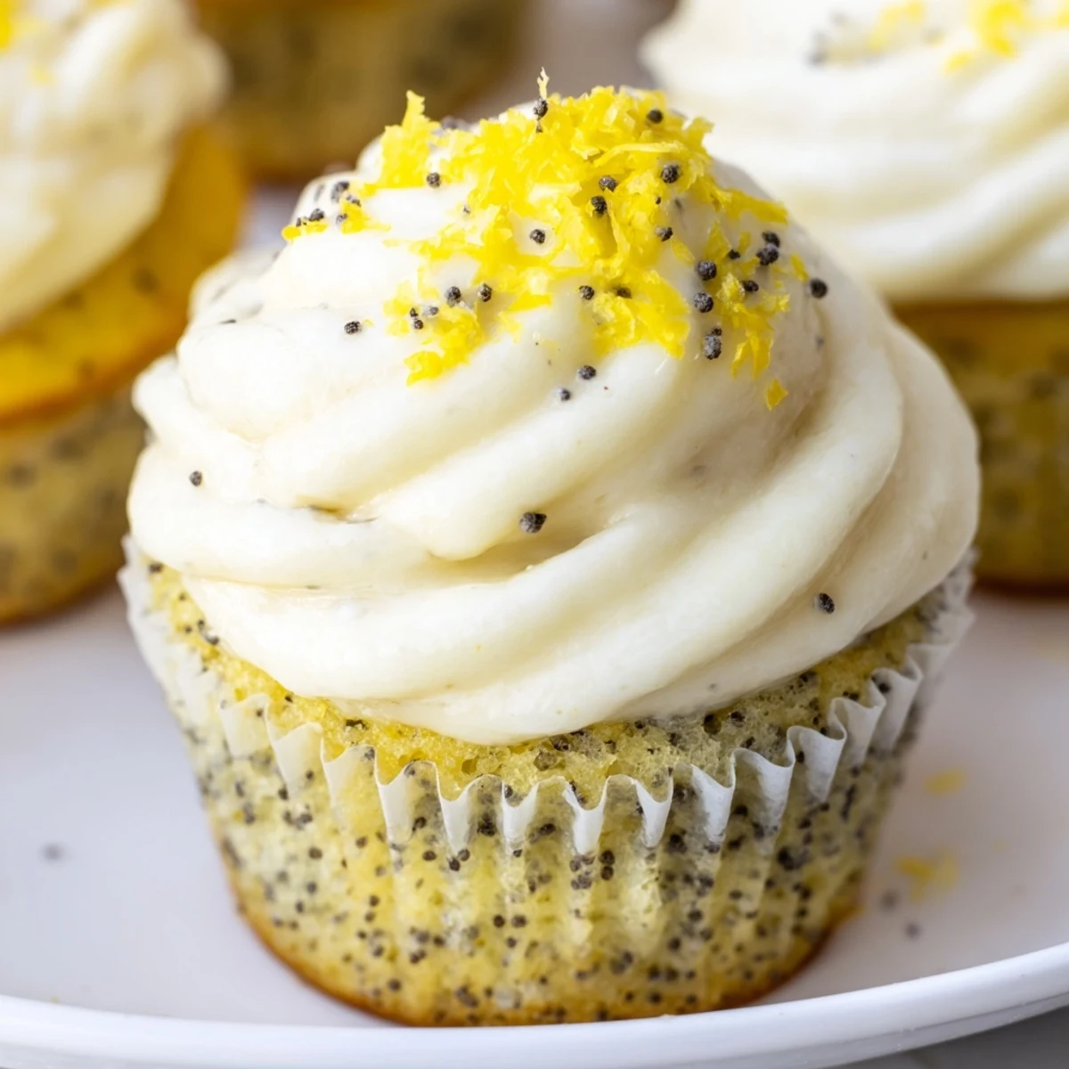 Freshly baked lemon poppy seed cupcakes with creamy white frosting and sprinkled lemon garnish
