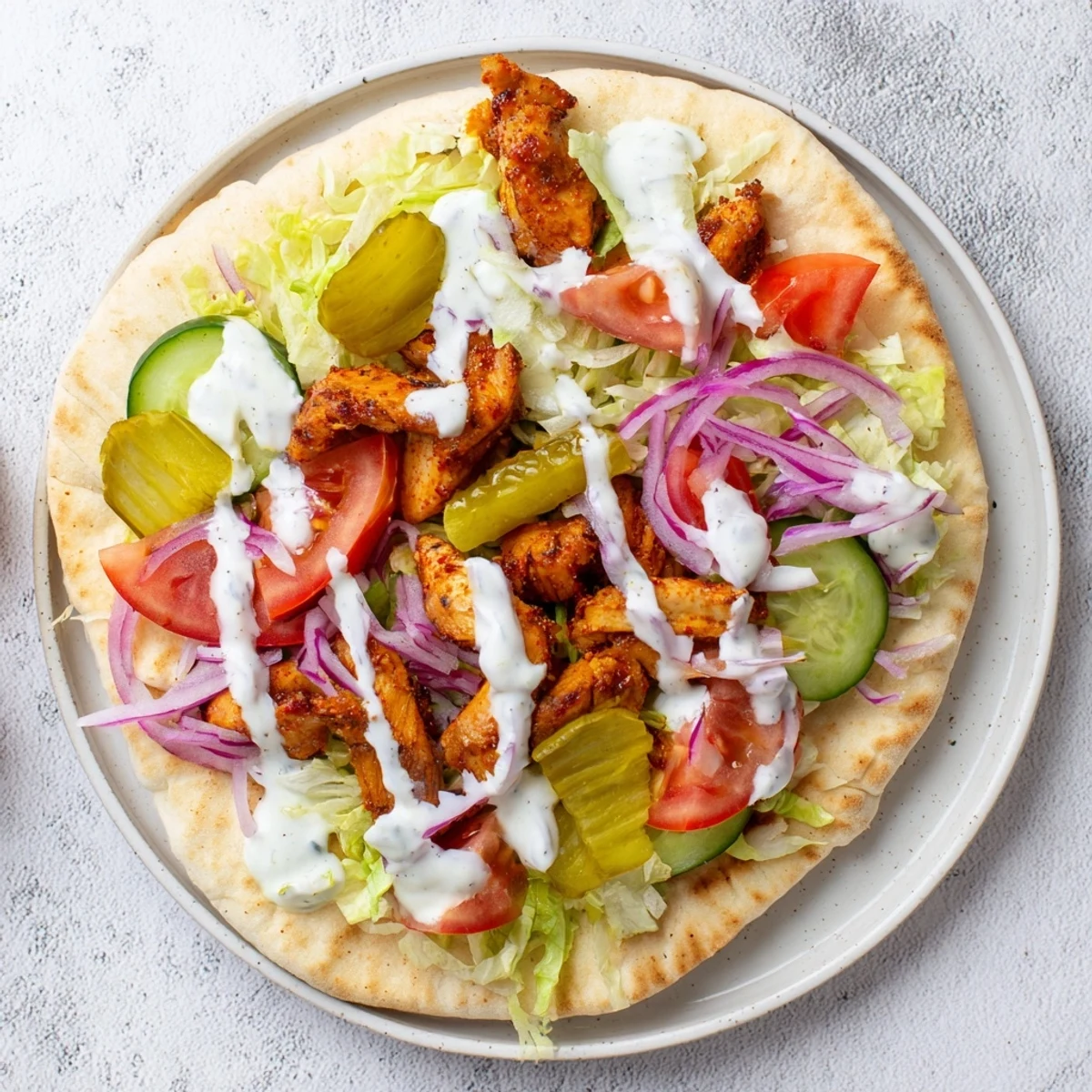 Middle Eastern chicken shawarma plated with colorful toppings pickles and drizzled tahini yogurt sauce