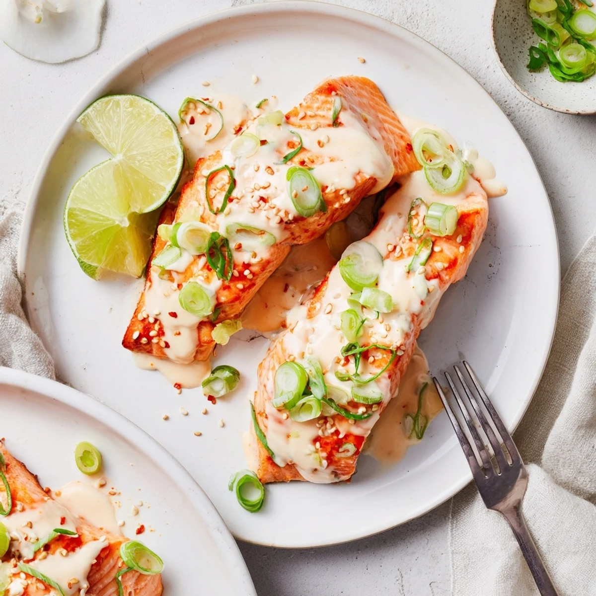 Tender baked Bang Bang Salmon fillets coated in creamy spicy red sauce with green onion garnish