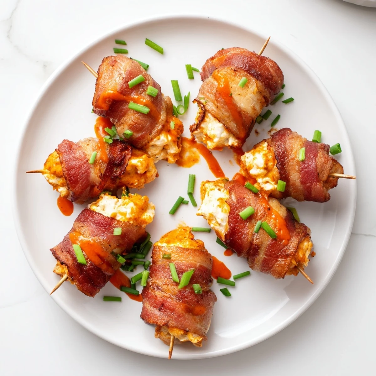 Oven-baked Buffalo Chicken Bombs garnished with fresh chives and drizzled with extra spicy sauce