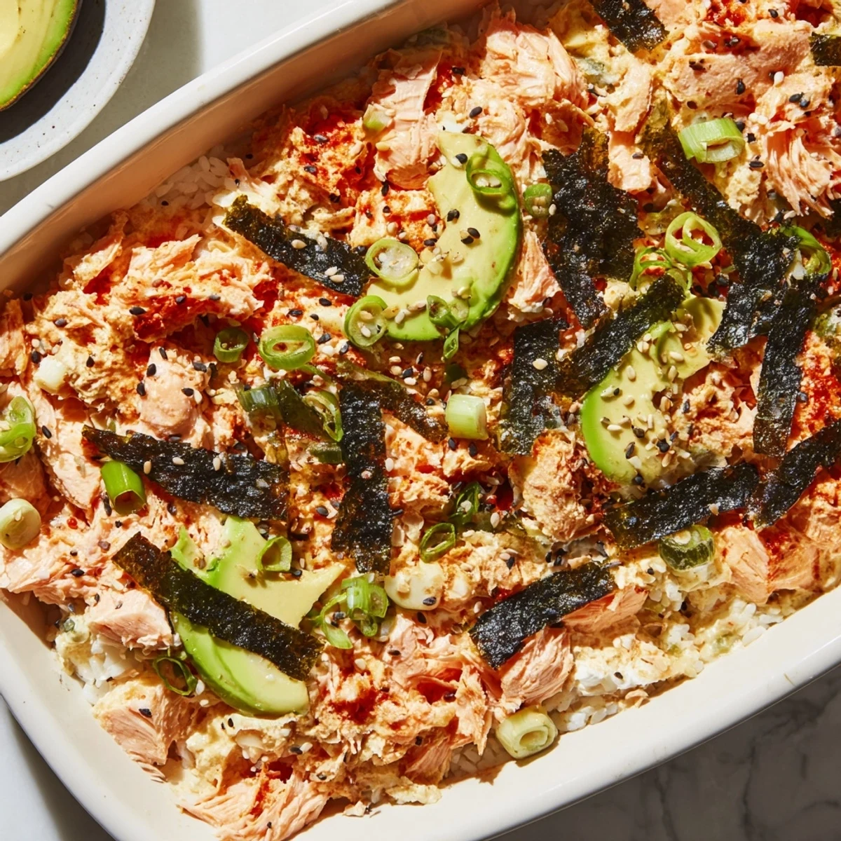 Flaky salmon and rice bake with creamy Sriracha mayo, nori strips, and sesame seed garnish