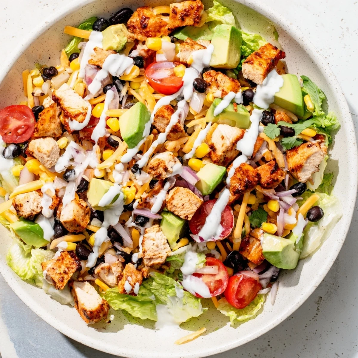 Protein-packed healthy BBQ chicken chopped salad served in a white bowl featuring charred grilled chicken pieces, cherry tomatoes, red bell pepper, fresh cilantro, and creamy lime barbecue dressing
