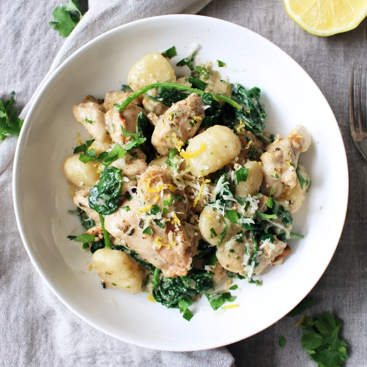 Creamy one pan lemon chicken gnocchi plated with wilted spinach and garnished with fresh parsley