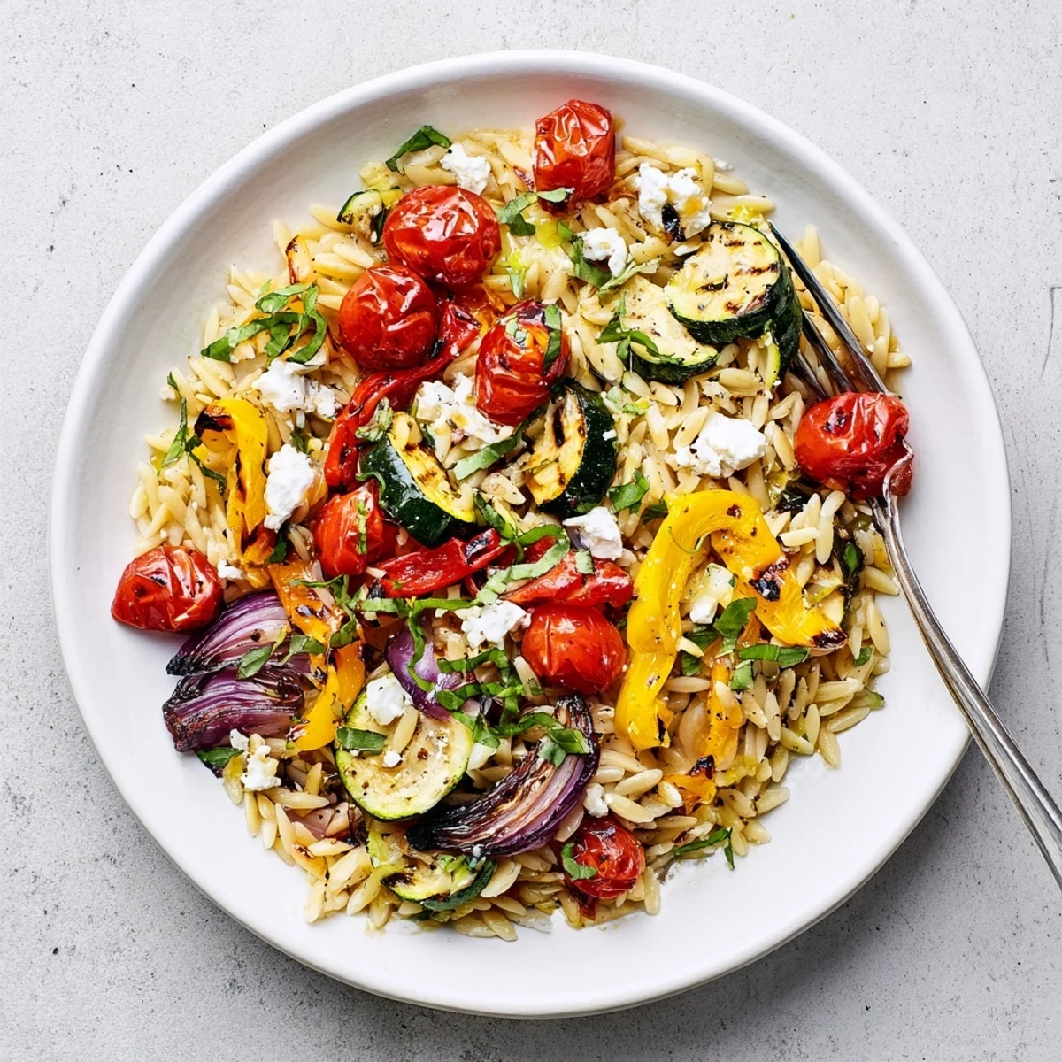 Golden roasted vegetable orzo with colorful peppers, zucchini, and crumbled feta garnished with fresh herbs