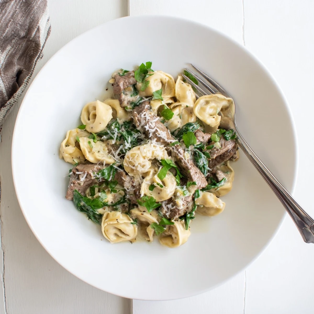 Golden seared steak strips and cheese tortellini swirl in a velvety garlic cream sauce topped with fresh parsley