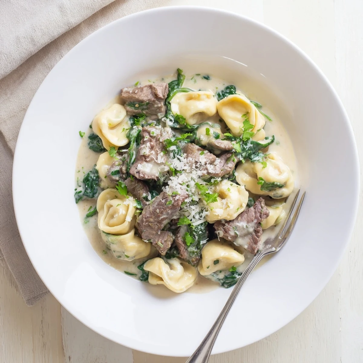 Plated garlic steak tortellini dish featuring tender beef, pillowy pasta, and wilted spinach in a rich Parmesan cream sauce