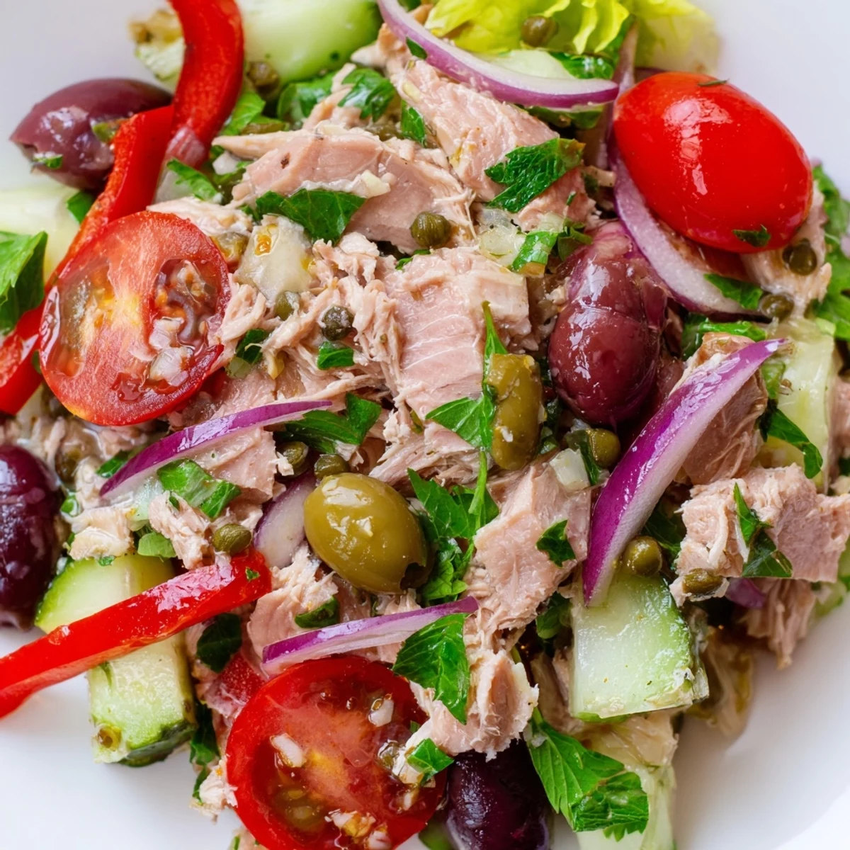 Mediterranean tuna salad in a white bowl with cherry tomatoes, olives, and fresh parsley