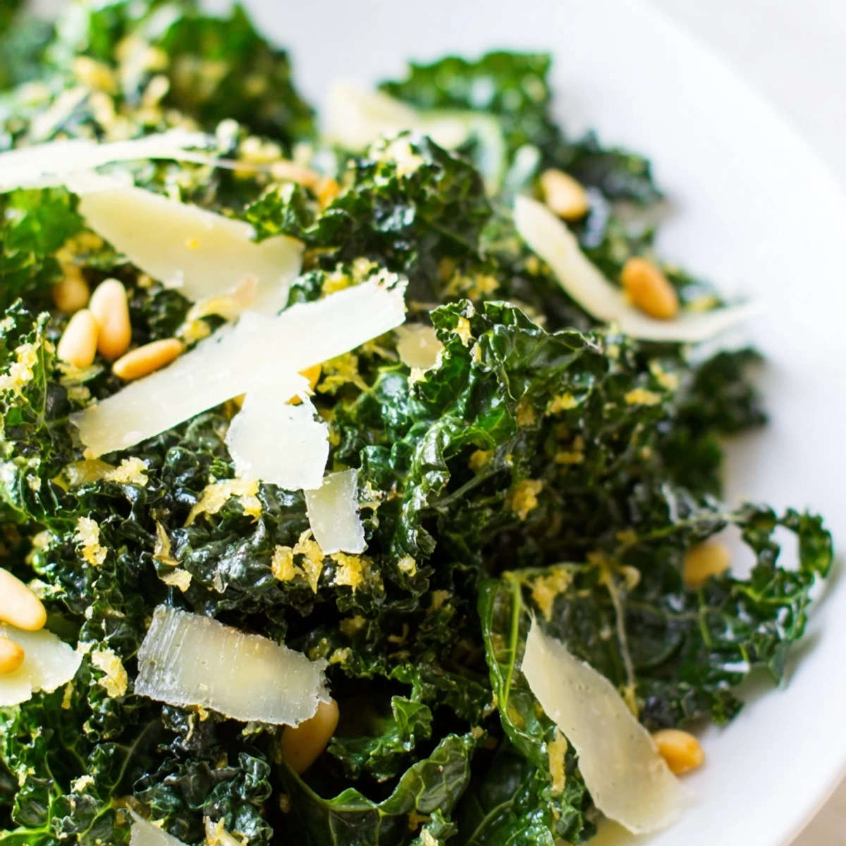 Bright green massaged kale leaves glistening with garlic lemon Parmesan dressing in a white serving bowl
