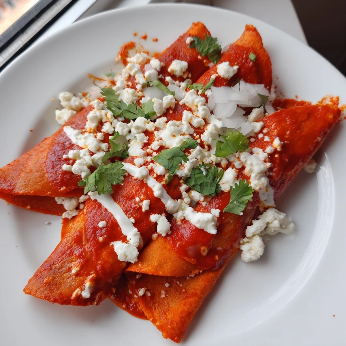 Warm entomatadas folded and smothered in vibrant red salsa with creamy drizzle and onions
