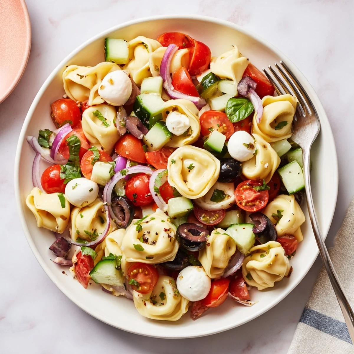 Colorful tortellini pasta salad in a white bowl with cherry tomatoes and cucumber