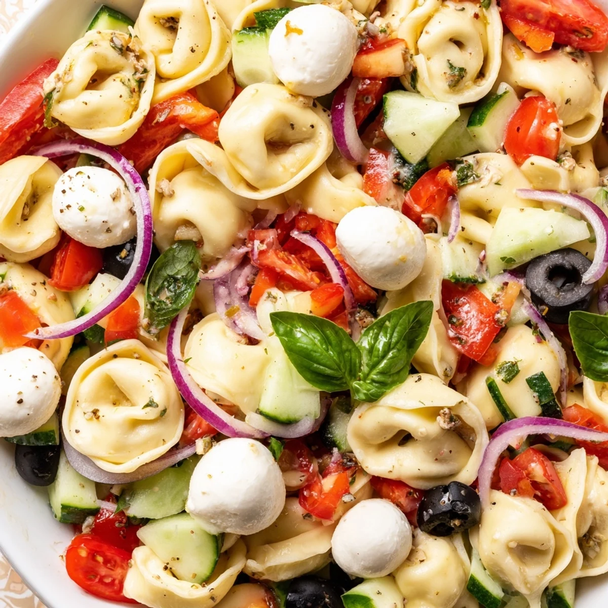 Colorful tortellini salad tossed with cherry tomatoes, cucumbers, and zesty Italian dressing in a white bowl