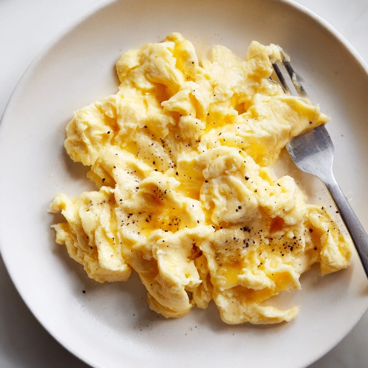 Velvety scrambled eggs topped with cracked pepper in a cast iron skillet