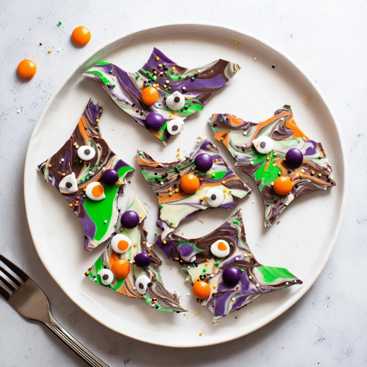 Melting Witches Bark with swirled chocolates, candy eyes, and colorful Halloween sprinkles on parchment paper