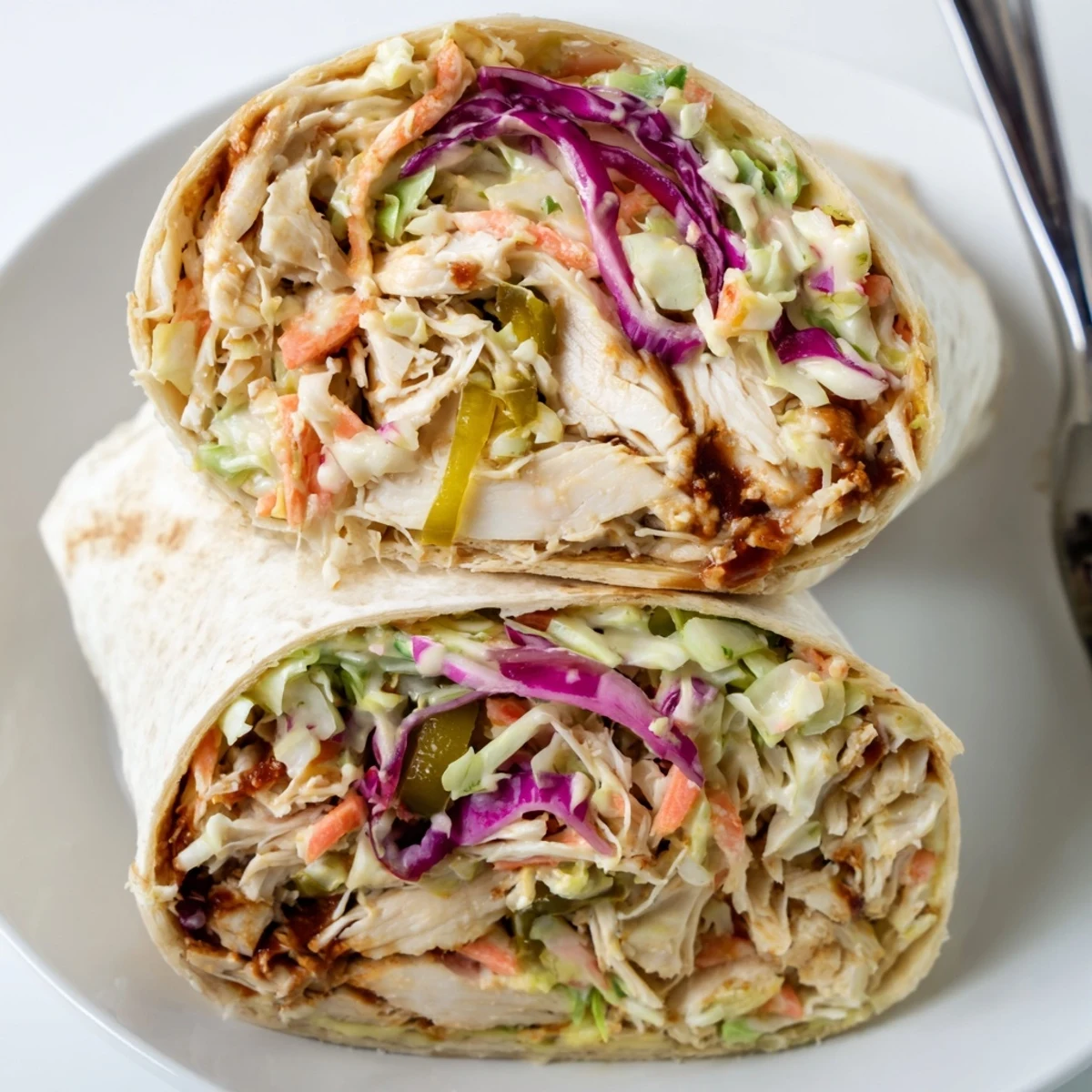 Two halved Bbq Chicken Coleslaw Wraps plated with tangy slaw and jalapeños  