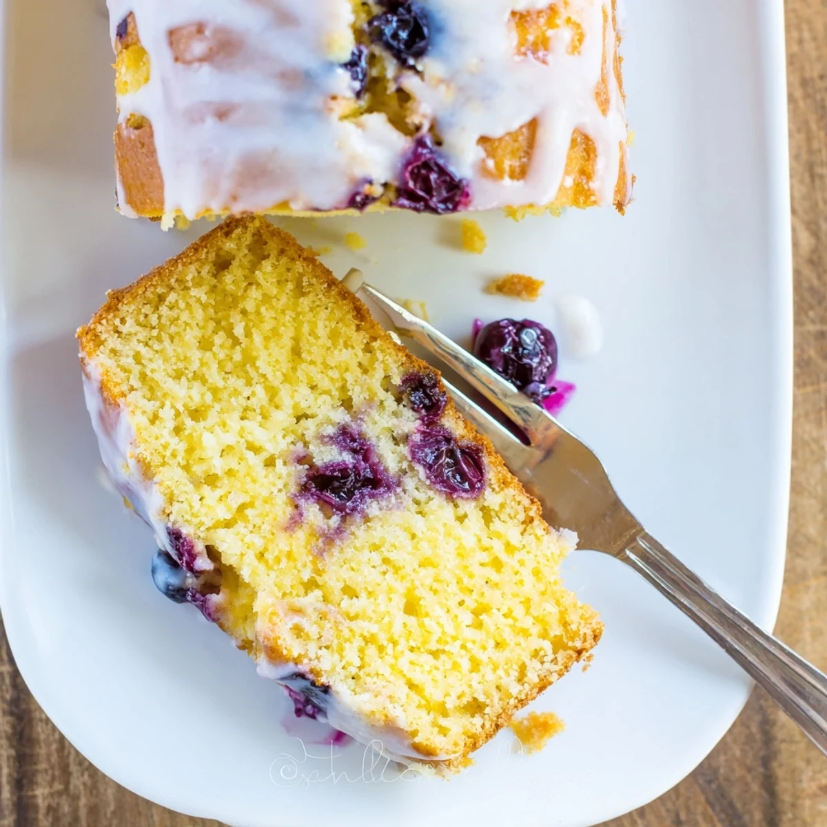 Golden lemon blueberry cake with bright citrus glaze and fresh berries scattered on top