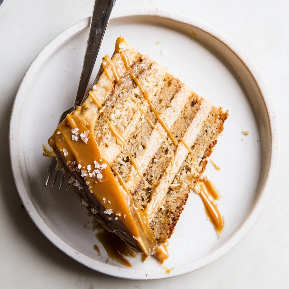 Slice of moist brown butter banana cake with caramel frosting and sea salt sprinkles on serving plate